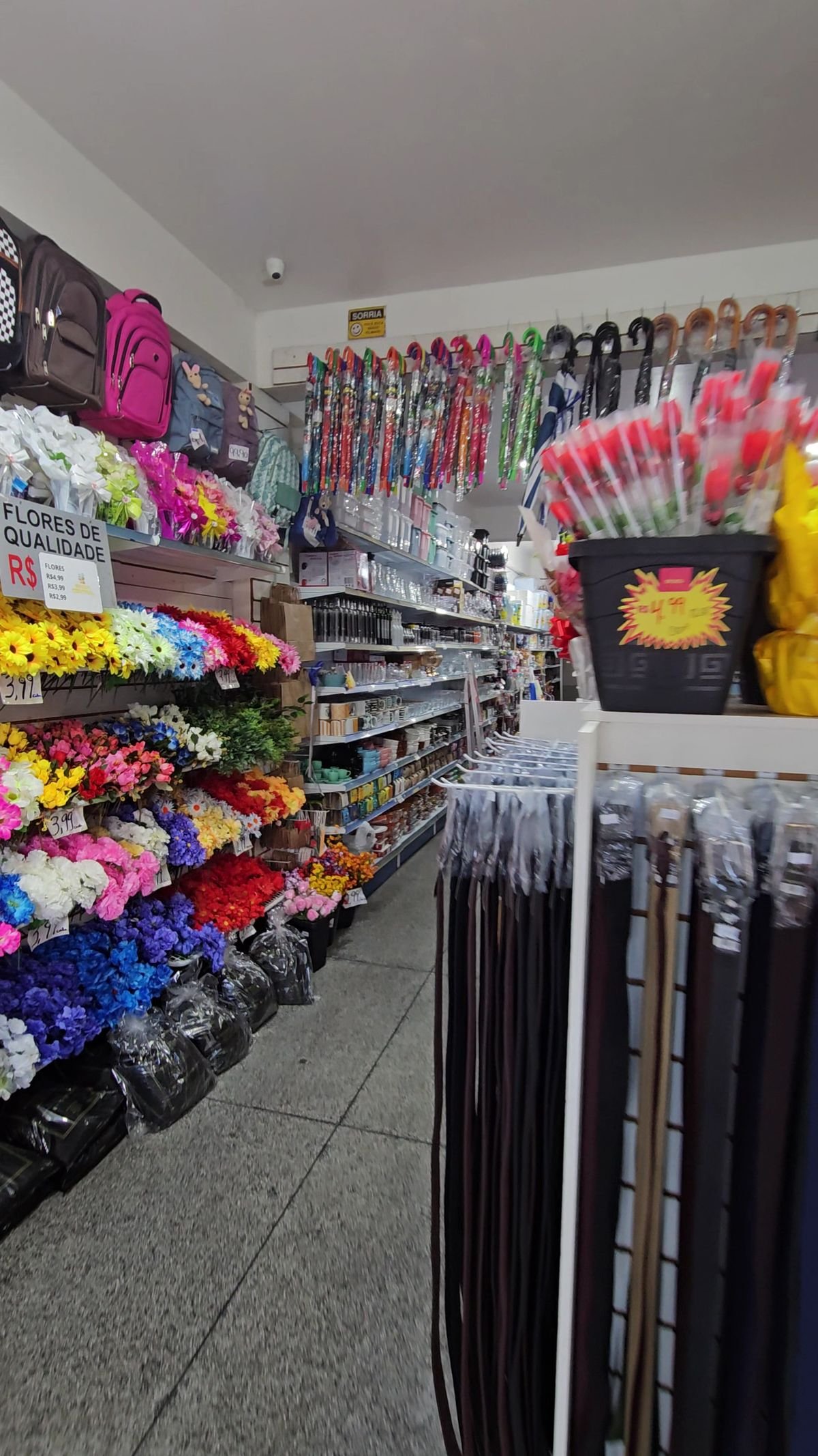 Corredor da loja com flores artificiais, bolsas, guarda-chuvas e cintos pendurados