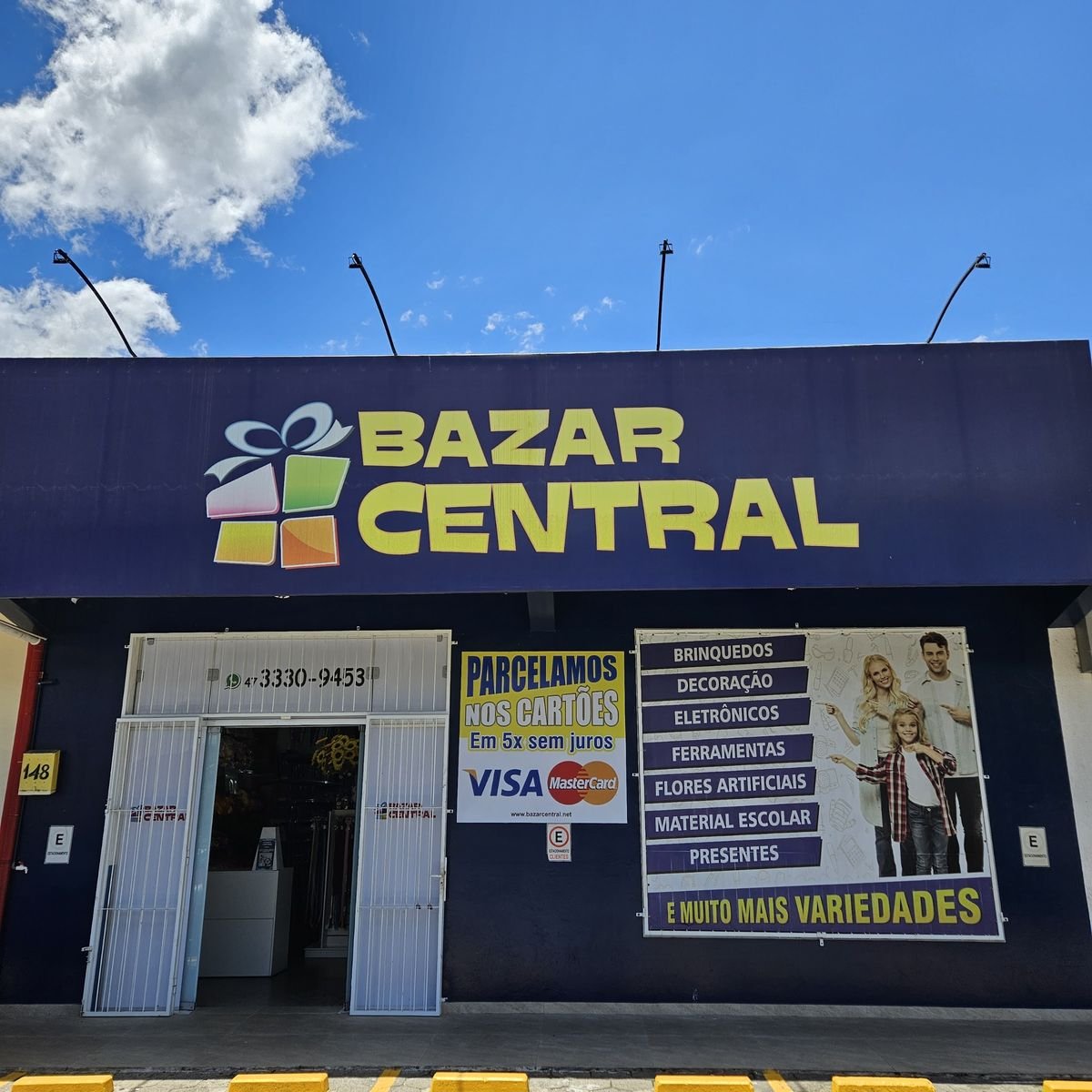 Fachada do Bazar Central: letreiro amarelo sobre fundo roxo e a lista de departamentos na vitrine